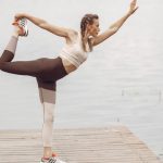 A woman stretches in a yoga pose on a wooden pier by a serene lake, showcasing flexibility and balance.